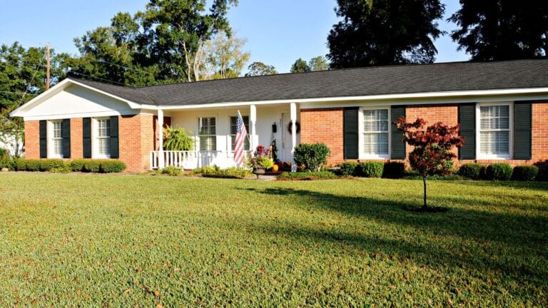 Single-story brick home with dark green shutters, a front porch and a large front lawn